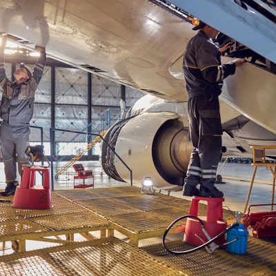 Full length side view portrait of men aviation mechanics fixing and checking spoiler and flaps on the airplane